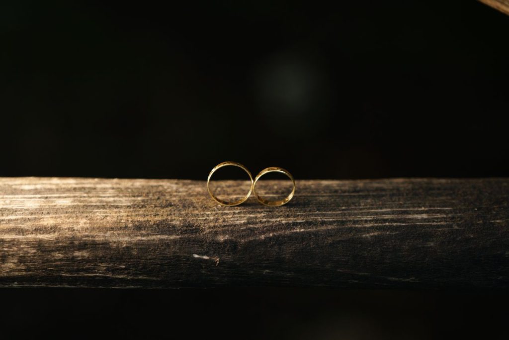 ACCUEIL Close-up of two gold wedding rings on rustic wood against a dark background.