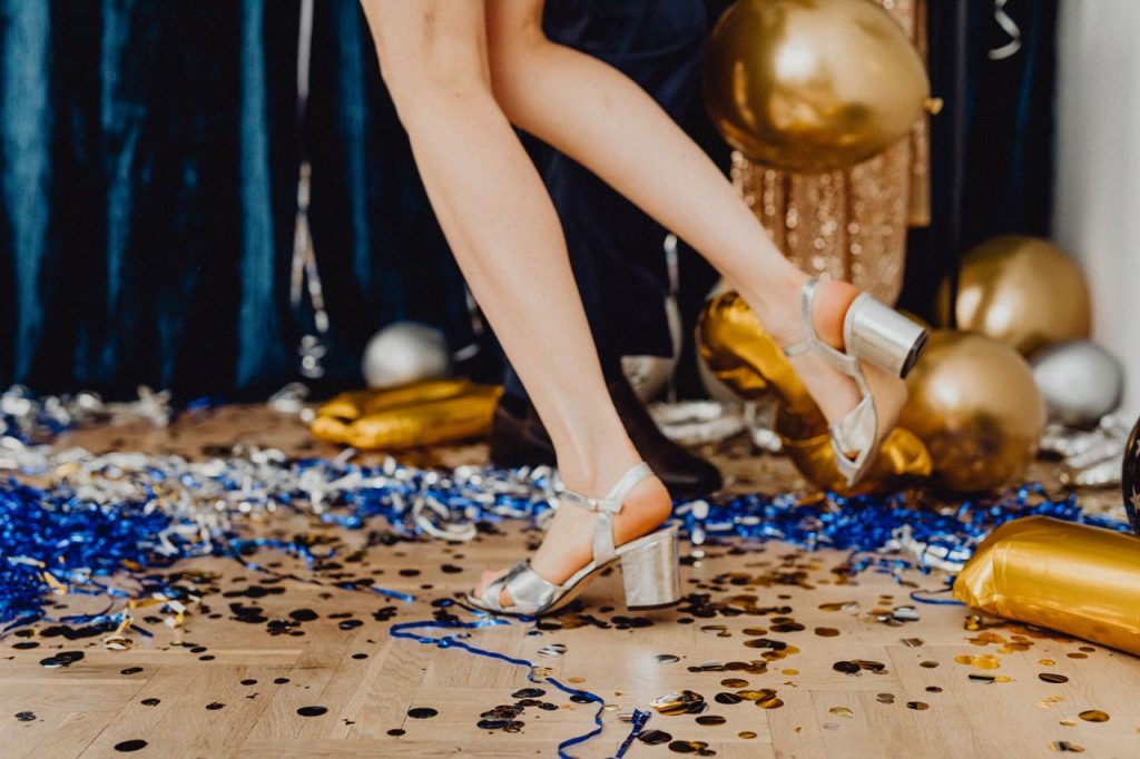 ACCUEIL Close-up of silver high heels amidst party decorations and confetti.